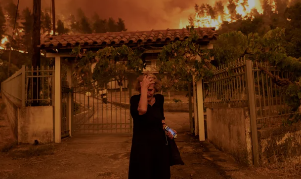Asszony a háza előtt, amelyet elér a tűz. Evia, Görögország. Foto: Bloomberg / Getty Images
